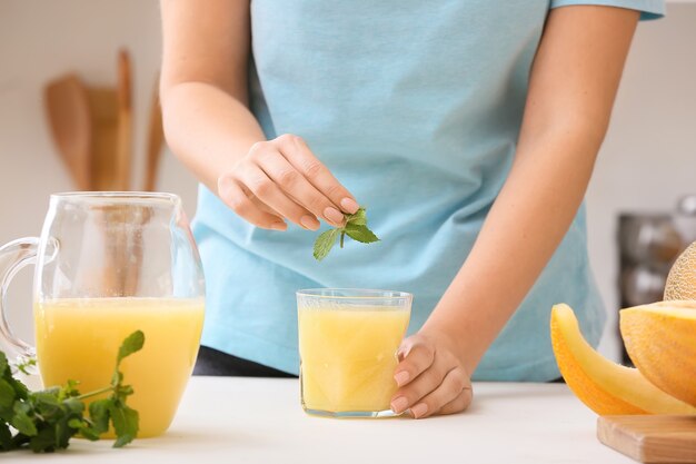 Mujer poniendo menta en vaso con batido de melón en la mesa de la cocina