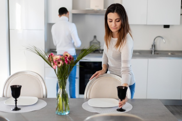Mujer poniendo la mesa mientras su novio está cocinando