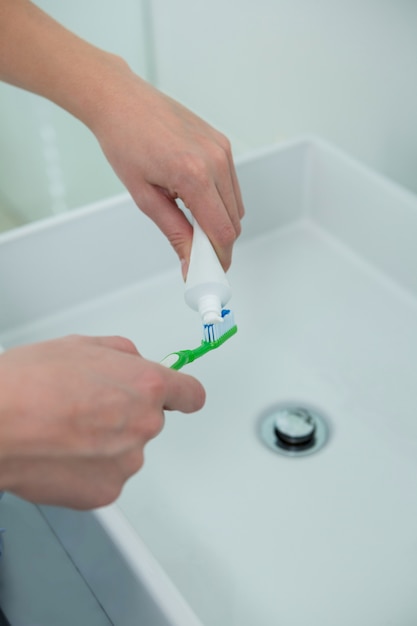 Mujer poniendo pasta de dientes en el cepillo en el baño.