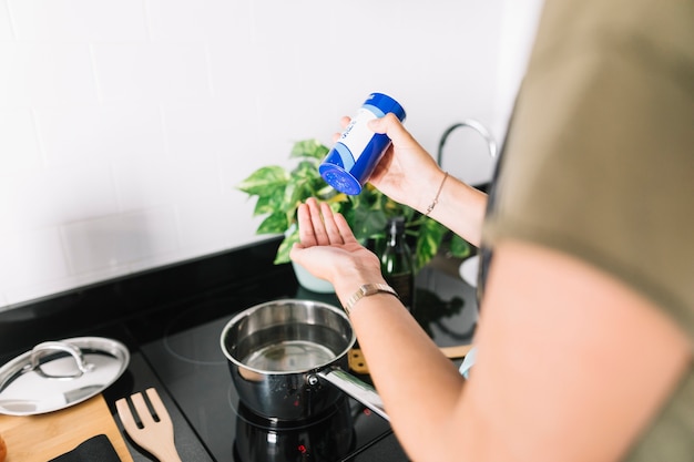 Foto mujer poniendo sal en la mano mientras se prepara la comida sobre la estufa de inducción