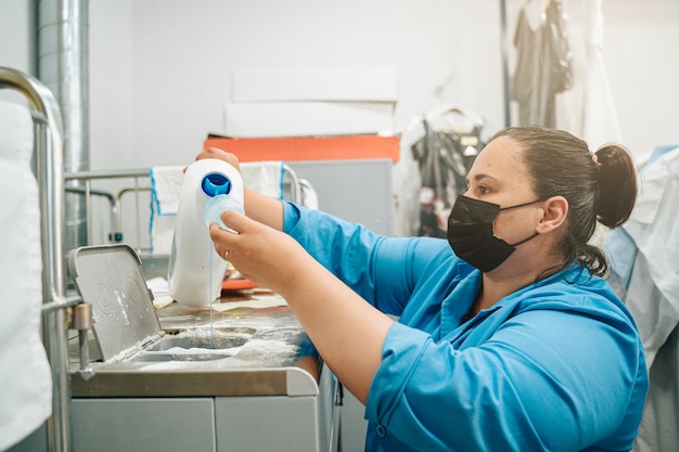 Mujer poniendo suavizante y detergente en la lavadora industrial