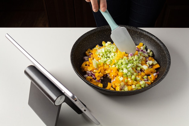 Mujer poniendo verduras en una olla y ver clase culinaria virtual. Clase de cocina online