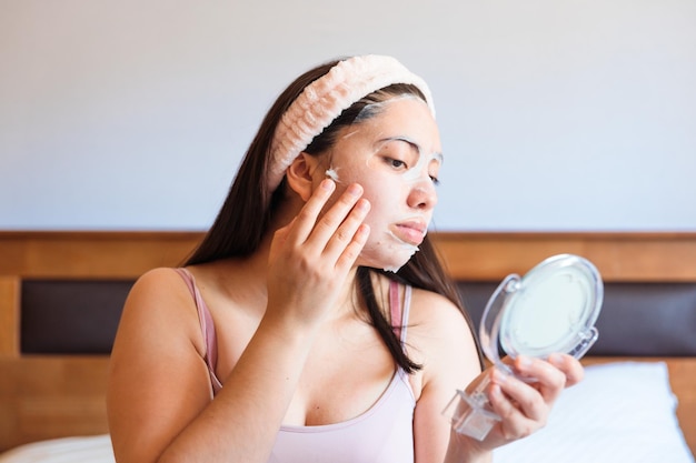 Una mujer poniéndose una mascarilla frente a un espejo