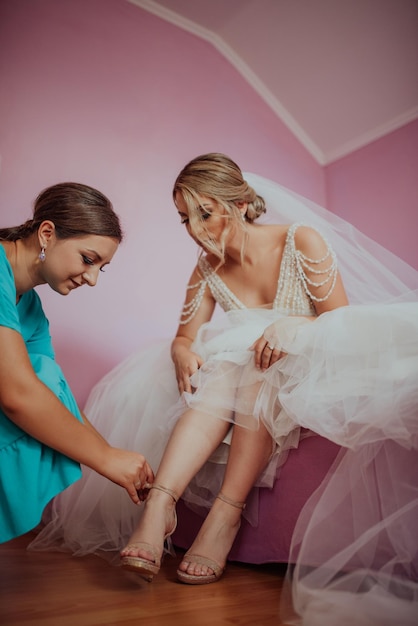 Mujer poniéndose los zapatos blancos de la novia el día de su boda Madrina ayudando a la novia con un vestido a ponerse los zapatos de tacón alto en los preparativos para realizar el sueño del matrimonio