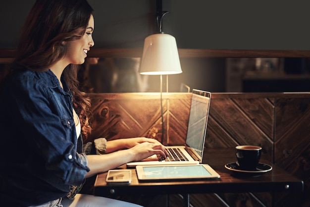 Mujer portátil y freelance por la noche en la cafetería redactora y investigación para la fecha límite del artículo Perfil de persona femenina y función de escritura para la columna en la planificación de cafeterías y en línea para el trabajo remoto
