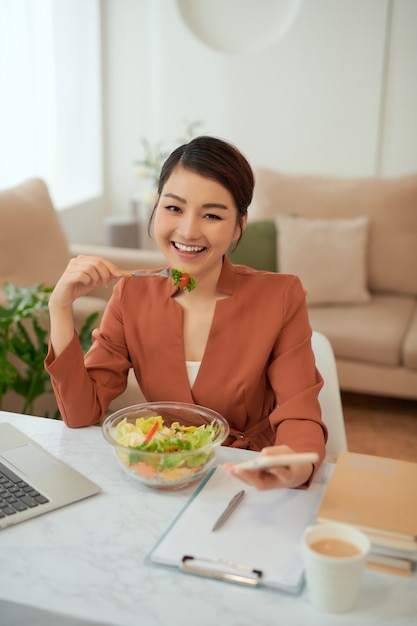 Mujer con portátil en el interior de la oficina moderna, almorzando.