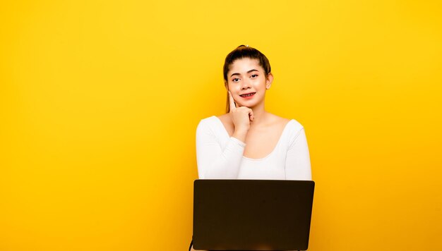 Mujer y portátil sentado felizmente sonriendo sobre un fondo amarillo