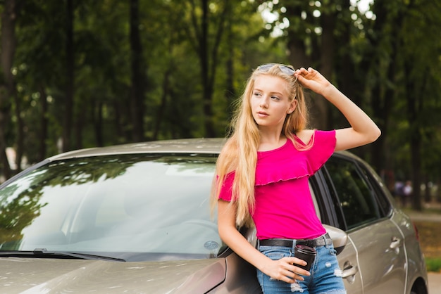 Mujer posa cerca del coche con gafas y copa