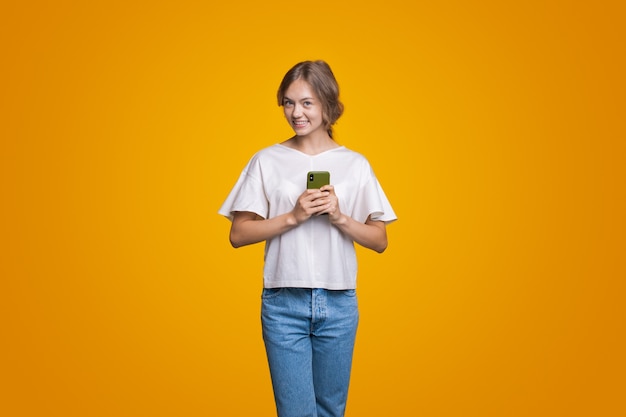 Mujer posando sonriendo a la cámara mientras escribe mensajes en el teléfono chica vestida con blusa blanca y j ...