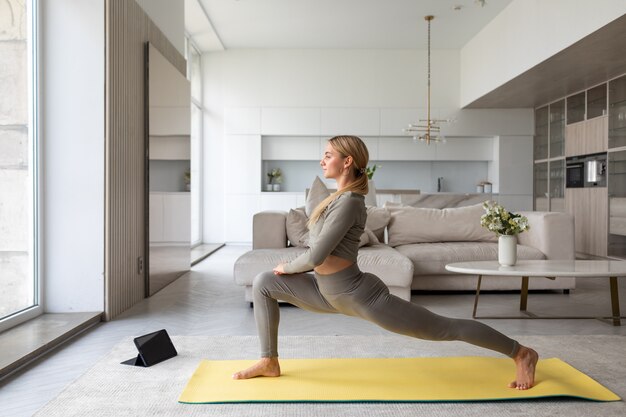 Una mujer se para en pose de yoga frente a la tableta viendo lecciones de yoga en casa