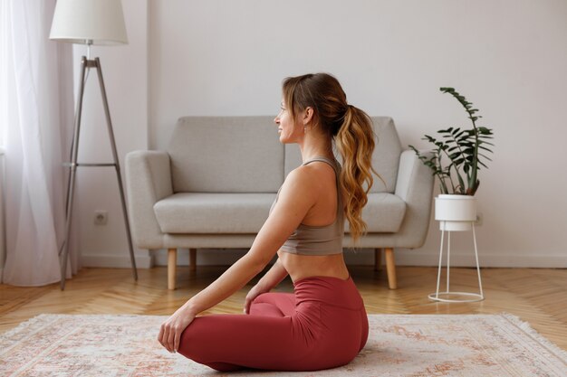 Mujer en pose de yoga de loto en casa en la sala de estar