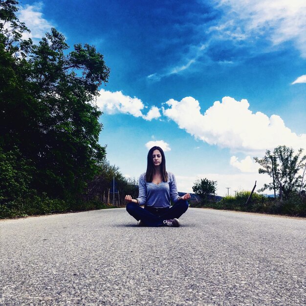 Foto mujer en posición de loto sentada en la carretera contra el cielo