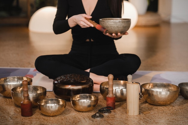 Una mujer en posición de loto usando un cuenco de canto en el interior Relajación y meditación Terapia de sonido medicina alternativa Prácticas curativas budistas