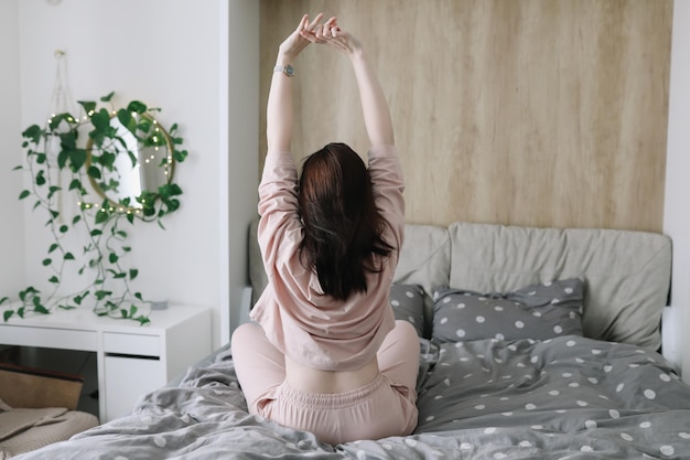 Mujer positiva con almohada sentada en la cama en casa Dulces sueños buenos días nuevo día concepto de vacaciones de fin de semana