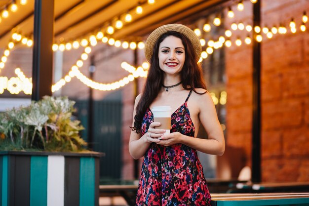 Mujer positiva con cabello oscuro y rostro atractivo, vestido con sombrero y vestido de verano