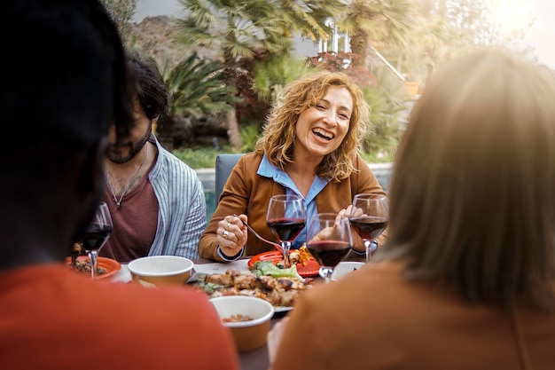 Una mujer positiva de cuarenta años sonríe, come bebidas y habla con amigos comiendo en la mesa de barbacoa en el patio de la casa de campo sentada en la mesa del brunch, comida y bebida, concepto de estilo de vida de la gente