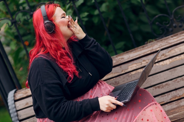 Mujer positiva de cuerpo de talla grande europea en un banco usando la computadora portátil