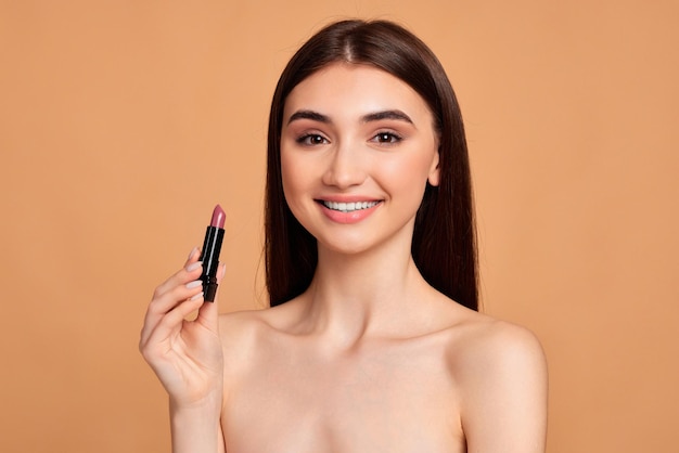 Mujer positiva feliz joven que sostiene el lápiz labial rosa