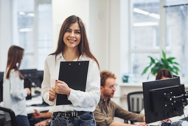 Mujer positiva de pie frente a jóvenes empresarios que trabajan juntos en la oficina moderna.