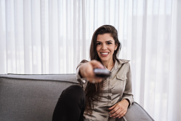 Una mujer positiva que sostiene el control remoto en el sofá.