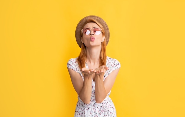 Mujer positiva con sombrero de paja y gafas de sol sobre fondo amarillo