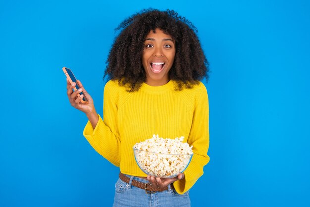 La mujer positiva sostiene un teléfono celular moderno conectado a los auriculares y aprieta el puño de las buenas emociones, excl.