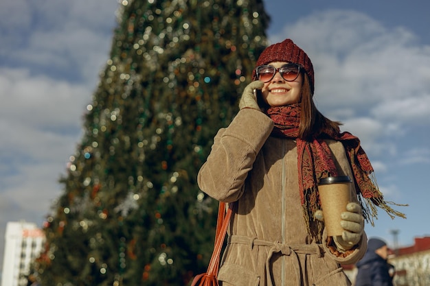 mujer positiva con taza de café para ir hablando por teléfono móvil