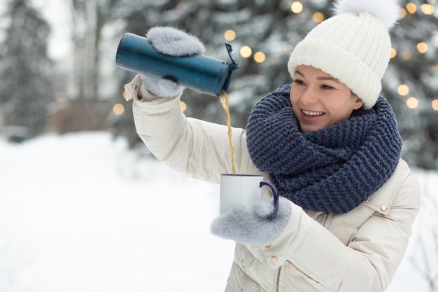 Mujer positiva vertiendo té de termo en el parque en invierno