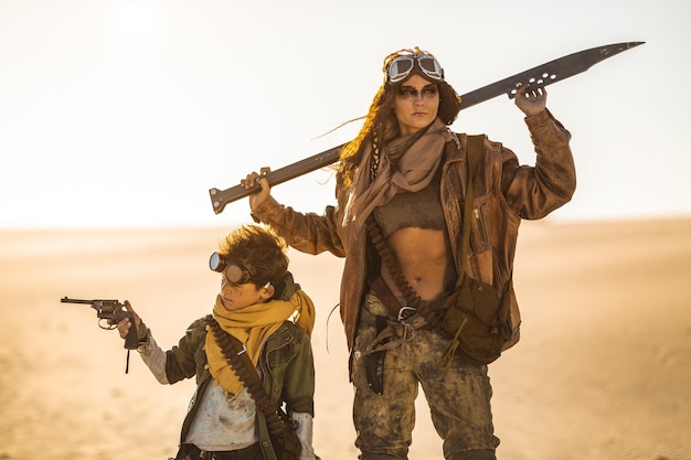 Mujer postapocalíptica y niño con armas al aire libre. Desierto y páramo muerto en el fondo