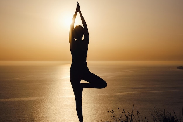 La mujer con la postura de yoga en la montaña al atardecer.