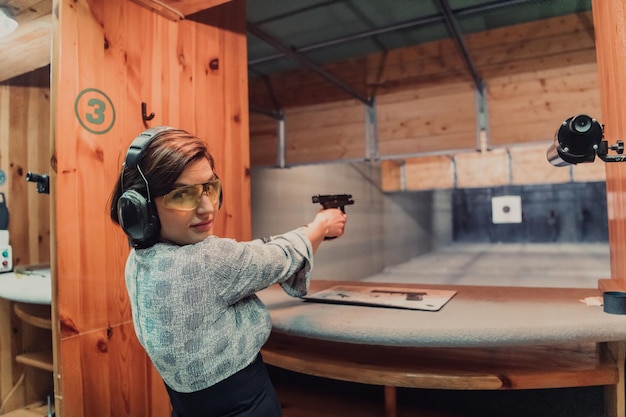 Una mujer practica disparar una pistola en un campo de tiro mientras usa auriculares protectores.