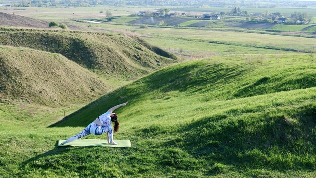 La mujer practica yoga deportiva en la naturaleza en primavera en verano en un día soleado Hombre mostrando su espalda en pose de yoga Cuerpo femenino sano en ropa deportiva