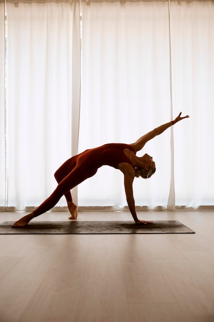 Una mujer practica yoga en una habitación blanca, está en pose de estrella de rock