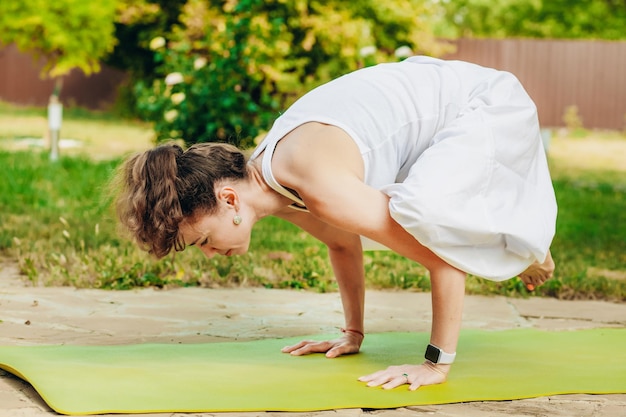 Mujer practica yoga en el jardín de verano Kakasana Crow Pose con brazos doblados