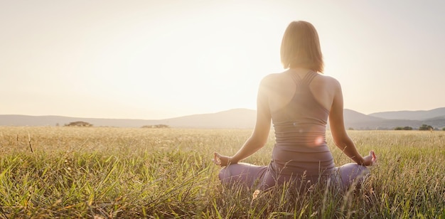 Mujer practica yoga y medita en posición de loto en el campo