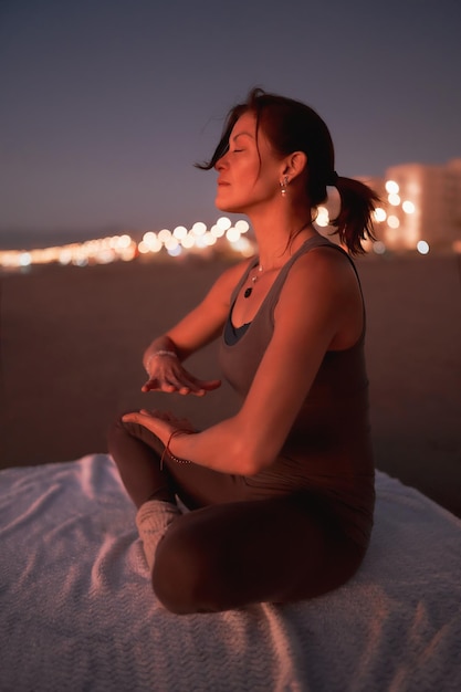 Mujer practicando reiki o meditación en la playa de la ciudad al atardecer