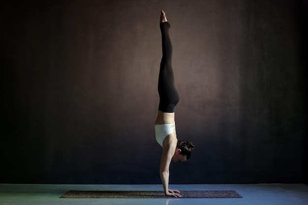 Mujer practicando yoga Adho Mukha Vrksasana ejercicio boca abajo pose de árbol