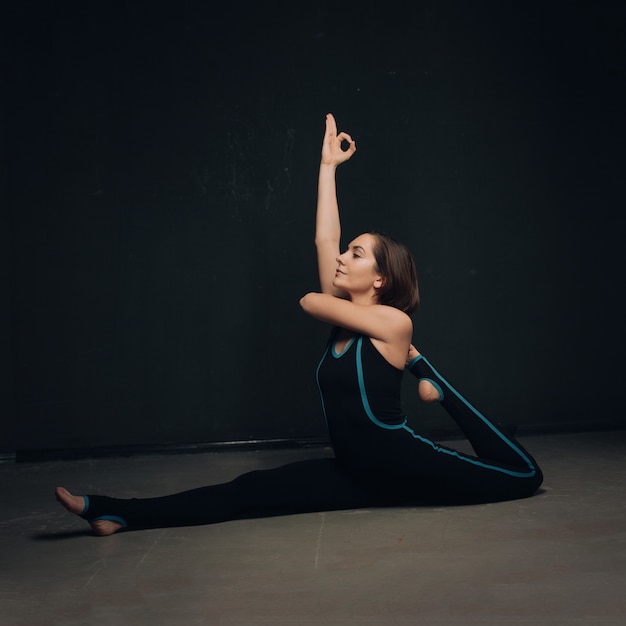 Mujer practicando yoga contra una pared oscura texturizada