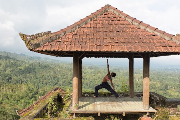 Mujer practicando yoga en la glorieta tradicional balinesa.