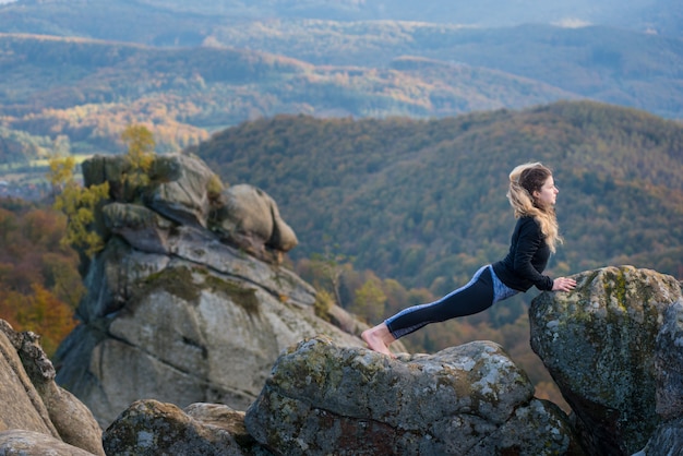 Mujer practicando yoga, haciendo asanas en la cima de la montaña.