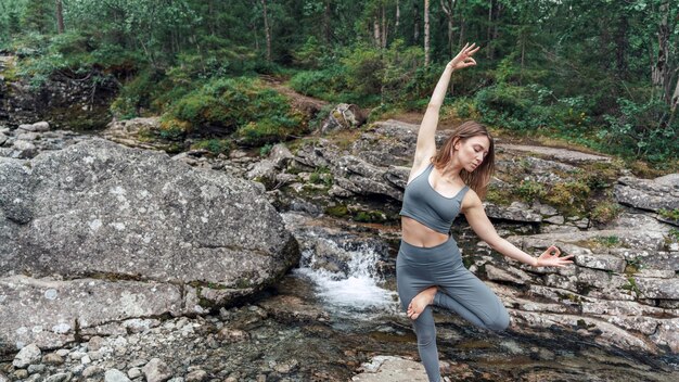 Mujer practicando yoga junto a un arroyo del bosque, una combinación perfecta de naturaleza y bienestar