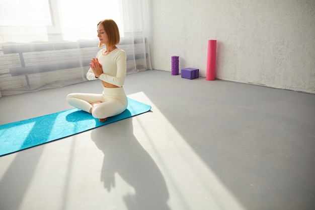 Mujer practicando yoga y meditación en postura de loto en una alfombra de yoga relajada con los ojos cerrados