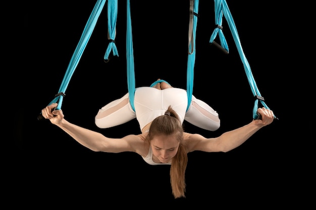 Mujer practicando yoga con mosca usando una hamaca suspendida del techo Chica gimnasta en clase de trapecio Fondo negro