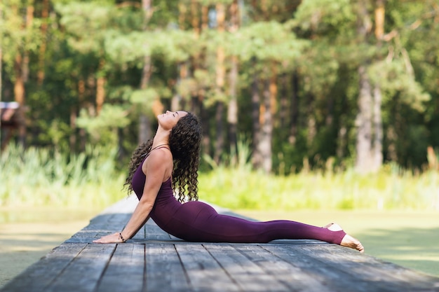 Mujer practicando yoga en el parque acostado sobre una estera realiza el ejercicio Bhujangasana