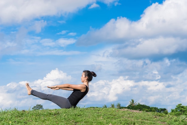 Foto mujer practicando yoga en el parque en la hierba verde con fondo hermoso cielo azul