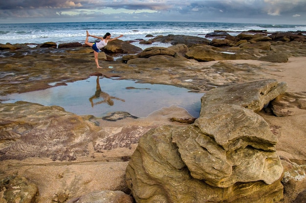 Mujer practicando yoga en una playa rocosa