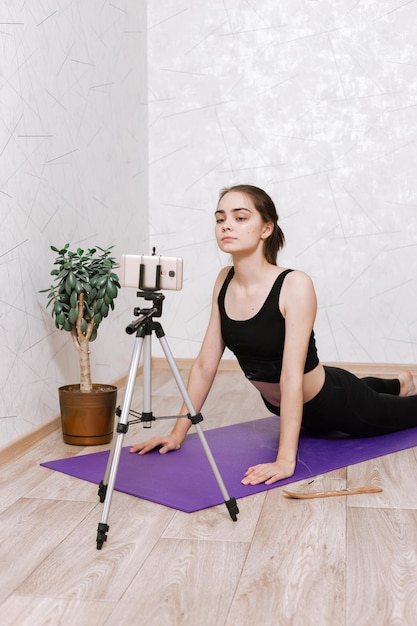 mujer practicando yoga en pose Cobra mientras ve una lección en línea en un smartphone