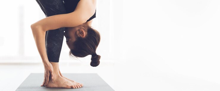 Mujer practicando yoga con una postura de flexión hacia adelante en una habitación luminosa