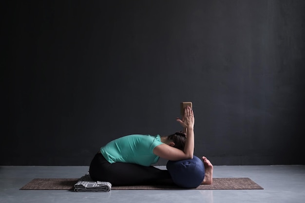 Mujer practicando yoga Postura de inclinación hacia adelante sentada usando bloque y refuerzo