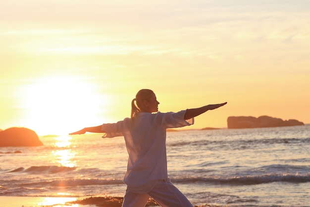 Mujer practicando yoga durante la puesta de sol en la playa